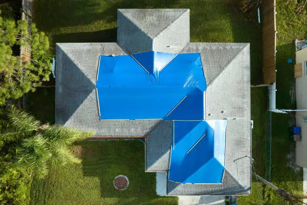Storm Damage Roof Repair Washington NC 5 Top-down aerial view of a home with blue tarps covering storm-damaged sections of its shingle roof