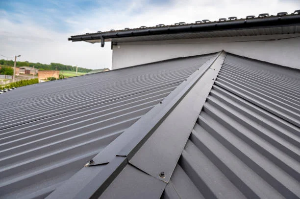 Dark gray ribbed metal roof panels with a fastened ridge cap on a residential home
