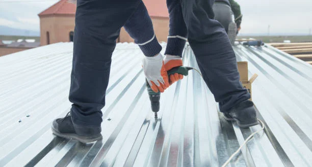 Roofer tightening screws with a drill on a corrugated metal roof during routine maintenance
