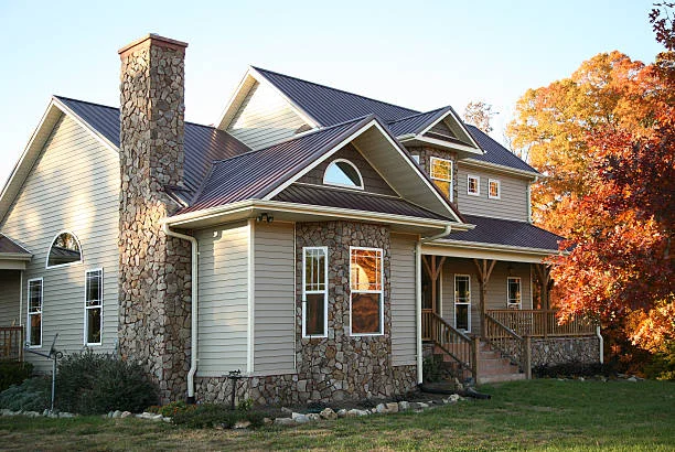 Burgundy standing-seam metal roof on a two-story home with stone chimney and fall trees