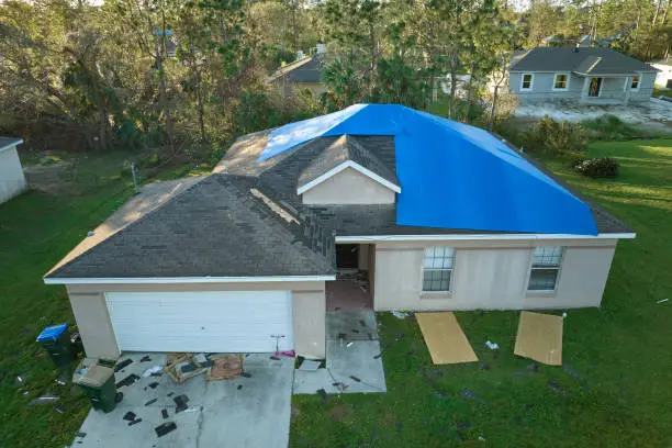 Storm Damage Roof Repair Washington NC 1 Storm-damaged home in Washington, NC with a blue tarp over the roof and torn shingles in the yard